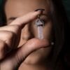 Човек държи между пръстите си заострена "Висулка за колие - Розов кварц" с акцент върху висулката.