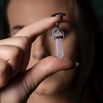 Човек държи между пръстите си заострена "Висулка за колие - Розов кварц" с акцент върху висулката.