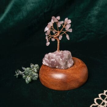 Декоративно от дърво Розов кварц със стебло от тел на дървена основа, добавено на фон от тъмнозелен плат с малко изкуствено растение до него.
