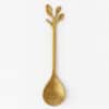 Златиста лъжичка за тамян има златисто покритие и дръжка с форма на три листа или клонки, заснети на обикновен бял фон.