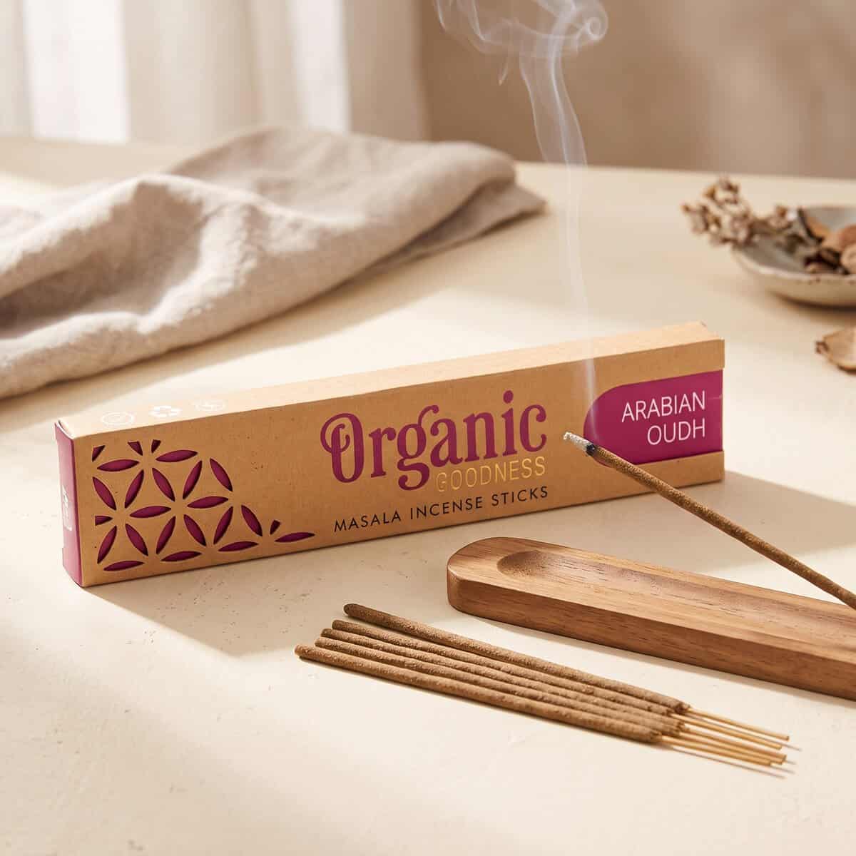 На дървена подставка до кутия с „Organic Goodness“ Ръчно изработени ароматни пръчици – Арабски оуд гори ароматична пръчица.